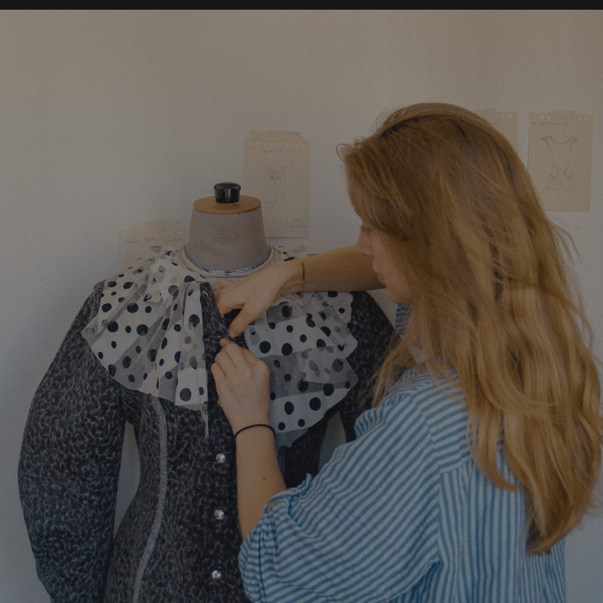 Créatrice de mode ajustant une collerette à pois sur une veste sur un mannequin de couture dans son atelier.